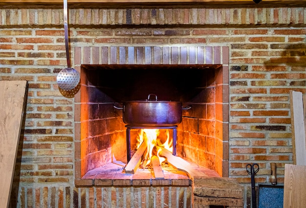 Panela de três pernas de ferro fundido em um fogo de madeira em uma chama de lareira de tijolos ao redor da panela