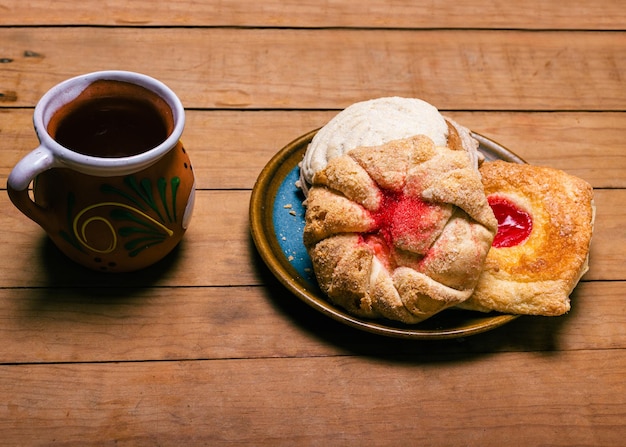 Panes dulces típicos mexicanos y taza de cerámica roja sobre mesa de madera Postres típicos mexicanos