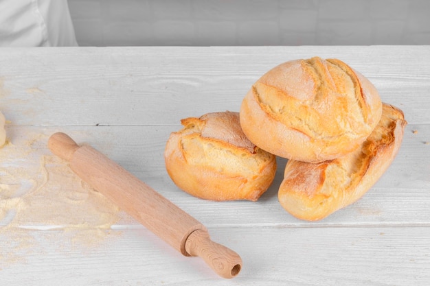 Panes de trigo italianos caseros frescos en la mesa con harina y masa sobre fondo blanco.