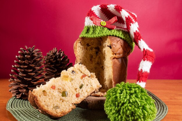 Foto panettone com chapéu de papai noel em mesa de madeira e fundo vermelho