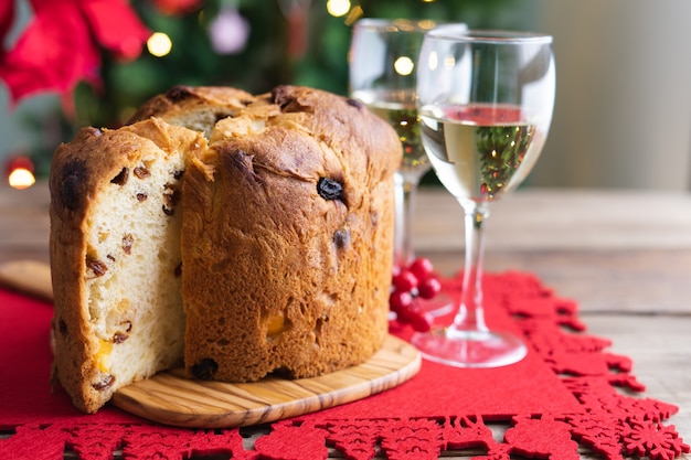 Panettone y copas de vino blanco en una mesa de madera con adornos navideños y árbol en el fondo ...