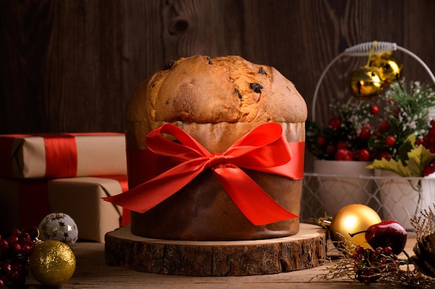 Panettone italiano tradicional de pastel de navidad con lazo rojo y decoración festiva en madera rústica