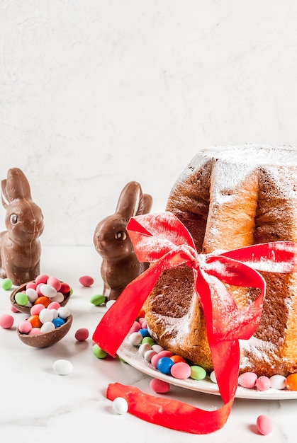 Foto panettone pandoro con festivo lazo rojo, conejos de pascua y dulces decoraciones de huevos de caramelo