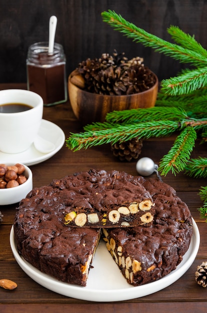 Panforte. Postre de Navidad italiano tradicional con nueces y frutos secos en una placa blanca sobre un fondo de madera oscura. Vertical, copie el espacio.