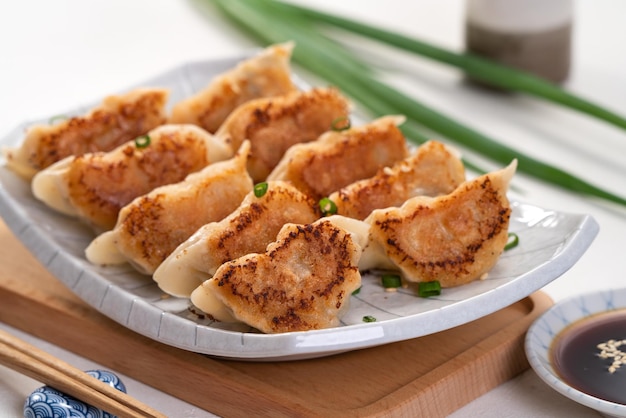 Panfried gyoza bolinho jiaozi em um prato com molho de soja no fundo da mesa branca