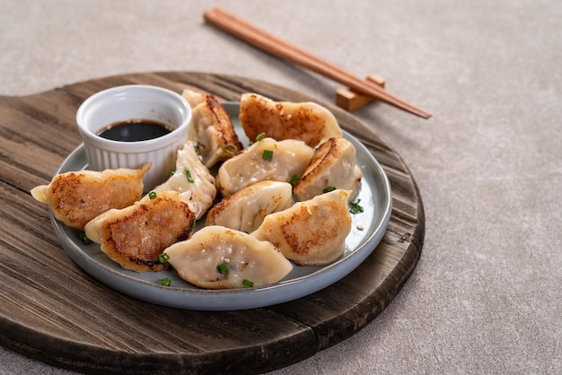 Panfried gyoza bolinho jiaozi em um prato com molho de soja no fundo da mesa cinza