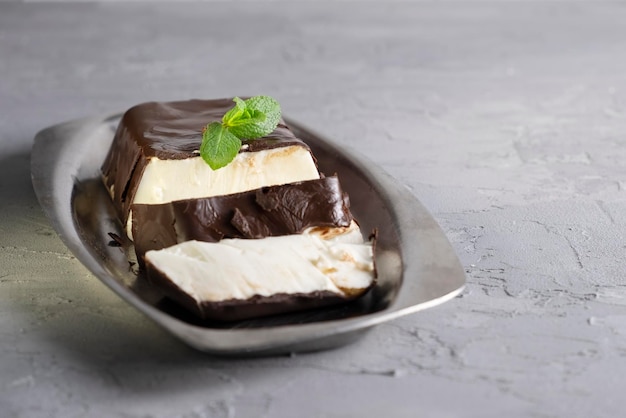 Panna cotta de sobremesa italiana servida em um prato branco com molho de chocolate e hortelã fresca em um fundo cinza claro no suporte de ferro