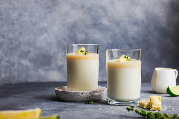 Panna cotta dietética cocinada con yogurt griego y leche de coco, cuajada de limón decorada con chocolate blanco y tomillo. Orientación horizontal con copyspace.