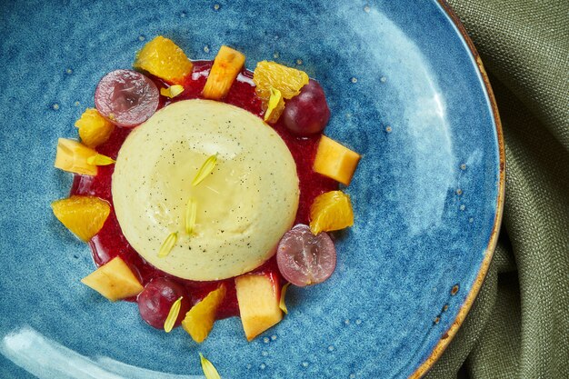 Panna Cotta - ein köstliches und schönes Dessert aus Sahne und Vanille mit Trauben und Pfirsich in einer blauen Schüssel auf einem Holztisch. Draufsicht, flache Lage, Kopierraum