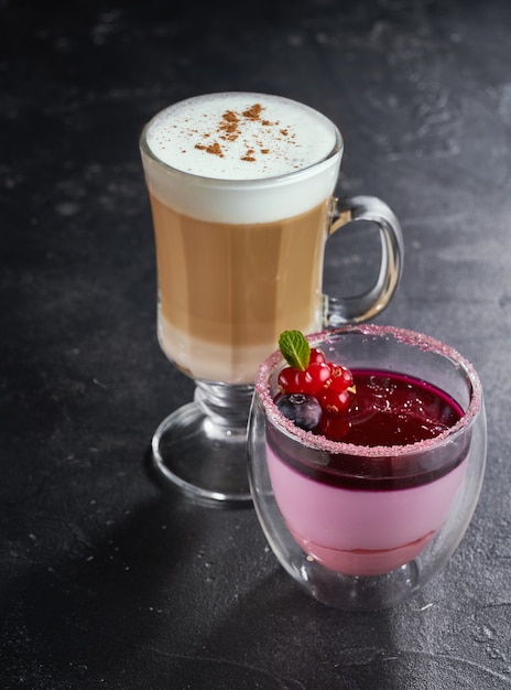 Panna cotta con frutos rojos en un vaso con café con leche sobre fondo oscuro.