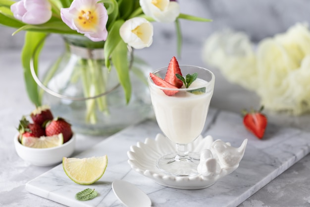 Panna cotta en vasos de vidrio con fresas sobre un fondo claro. Ramo de tulipanes sobre una mesa blanca.