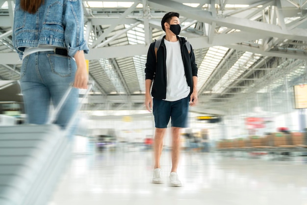 Pano casual de treveller masculino asiático inteligente atraente usa máscara facial protetora preta andando no terminal do aeroporto