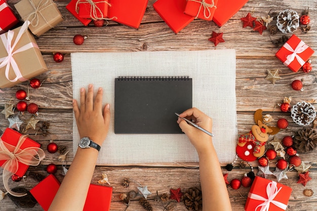 Paño de mesa de madera y la joven que estaba tomando notas arriba del concepto de diseño de fondo de Navidad decoración de vacaciones composición de ornamentos con caja de regalos de Navidad renos estrella