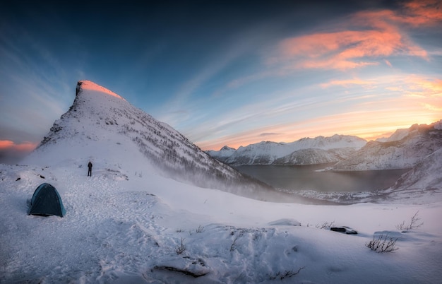 Panorama del amanecer sobre la cordillera nevada con una tienda de montañeros acampando en invierno en el monte Segla en la isla Senja