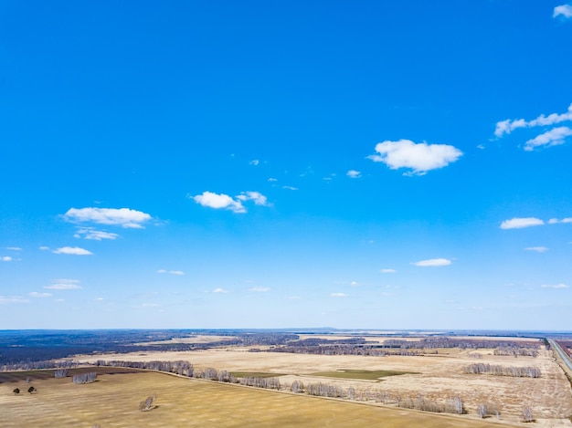 Panorama aus der Luft auf die üppigen Wiesen und Felder mit bunten Parzellen landwirtschaftlicher Nutzpflanzen vor der Aussaat im Frühling außerhalb der Stadt in der Sonne unter blauem Himmel und weißen Wolken. Natur in der Saison