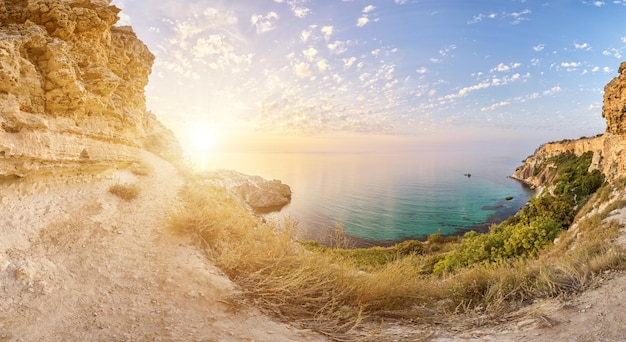 Panorama bei Sonnenuntergang mit schönen Wolken in der felsigen Bucht mit kristallklarem azurblauem Meer auf a