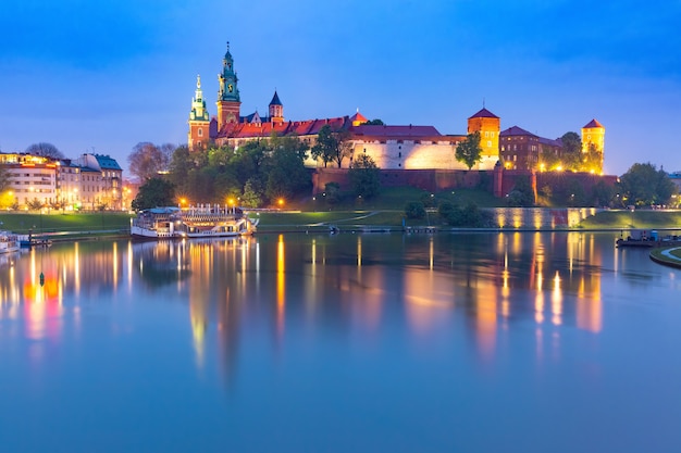 Panorama del castillo de Wawel en la colina de Wawel con reflejo en el río por la noche, Cracovia, Polonia