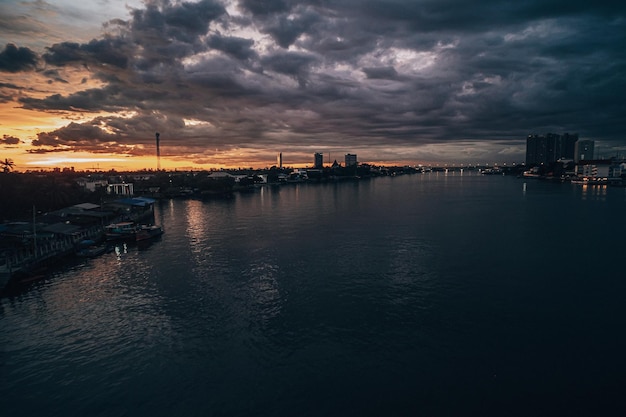 Panorama Cityscape al atardecer con un gran río en primer plano y nubes de tormenta en el fondo