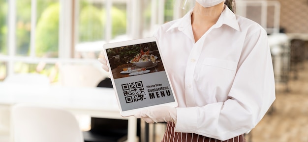 Panorama close up garçonete com máscara facial e protetor facial segurar tablet digital com código QR para o cliente verificar o menu sem contato online Conceito de tecnologia e contato sem contato para o novo restaurante normal