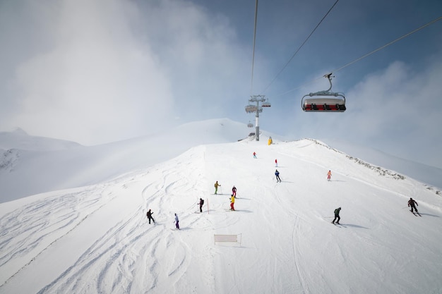 Panorama da encosta da estação de esqui pessoas no elevador esquiadores e snowboarders na pista com