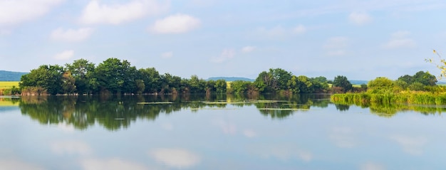 Panorama da paisagem de verão com rio e árvores refletidas na água do rio