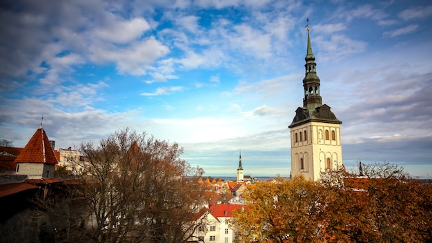 Panorama de outono de Tallinn da muralha da fortaleza. Vista da torre da igreja, árvores de outono e a muralha da fortaleza. Céu azul texturizado com nuvens