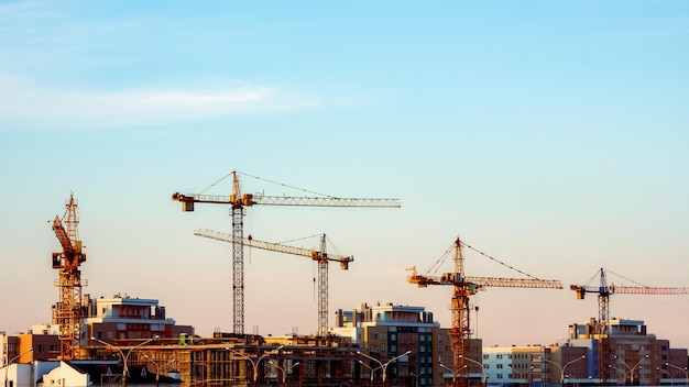 Panorama de um canteiro de obras Muitos guindastes de torre no fundo do céu azul da noite Cores quentes