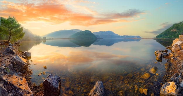 Panorama de um lago de montanha com uma costa rochosa ao pôr do sol