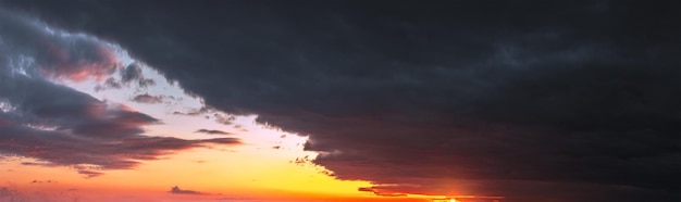 Panorama des dramatischen farbenfrohen Sonnenuntergangs mit dunklen und hellen Wolken. Die Sonnenstrahlen brechen durch den bewölkten Himmel. Dunkle Wolken vor einem hellen gesättigten Himmel.