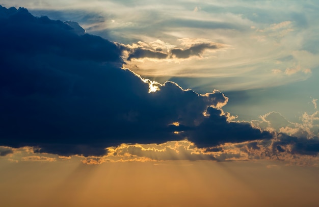 Panorama des Himmels bei Sonnenaufgang oder Sonnenuntergang. Schöne Ansicht der dunkelblauen Wolken beleuchtet durch hellorange gelbe Sonne auf klarem Himmel. Schönheit und Kraft der Natur, Meteorologie und Klimawandel.