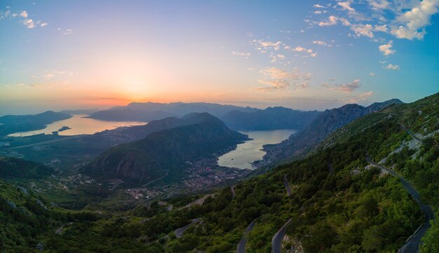 El panorama del deslumbrante sol en el cielo nocturno ilumina todos los picos de las montañas balcánicas montenegrinas y la costa de la bahía de Kotor