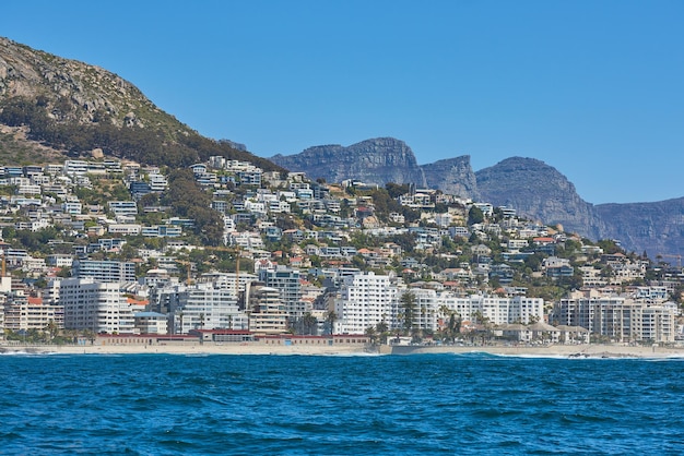 Panorama do mar com céu azul de nuvens e prédios de apartamentos de hotel chique ao fundo Sea Point com os Doze Apóstolos e o Parque Nacional Table Mountain na Cidade do Cabo, África do Sul