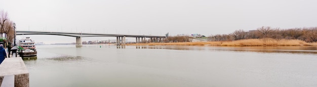 Panorama-Flusslandschaft bei bewölktem Wetter Dampfer am Pier Autobrücke über den Fluss Reisen und Wandern bei jedem Wetter