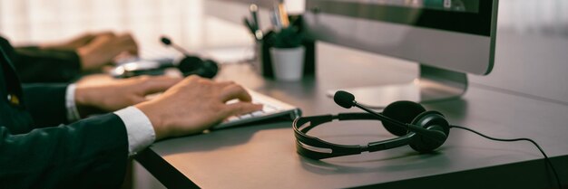 Foto panorama-fokus-headset auf dem schreibtisch des call-center-arbeitsplatzes mit unscharfem hintergrund des operator-teams oder telesales-vertreters, der sich mit der bereitstellung von kundenbetreuungsdiensten für kunden oder dem verkauf von prodigy beschäftigt