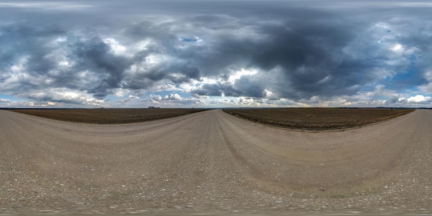 Panorama hdri esférico completo sem costura vista de ângulo de 360 graus na estrada de cascalho entre campos em dia de primavera com nuvens de tempestade antes da chuva em projeção equirretangular pronta para conteúdo VR AR