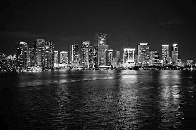 Panorama del horizonte de la ciudad de Miami por la noche, EE. UU. Iluminación de rascacielos que se refleja en el agua del mar al atardecer Diseño de estructura de arquitectura Desarrollo de construcción de edificios Descubrimiento de viajes de pasión por los viajes