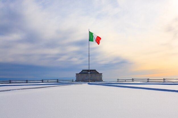 Panorama de invierno de los Alpes italianos. Edificio conmemorativo de la primera guerra mundial. Bandera italiana ondeando