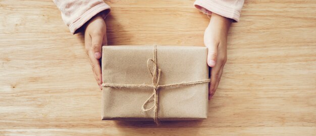 Panorama de la mano de niña con caja de regalo sobre fondo de mesa de madera