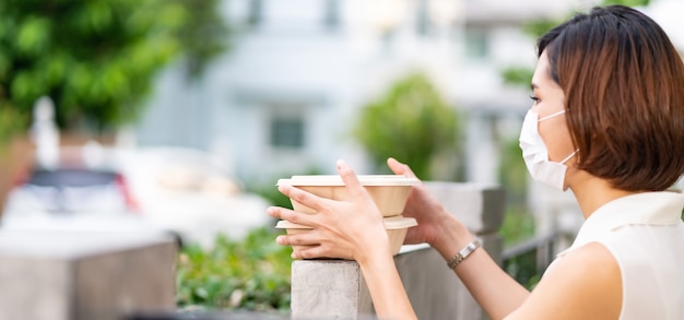 Panorama mujer asiática con mascarilla cliente tomar entrega de cajas de comida sin contacto