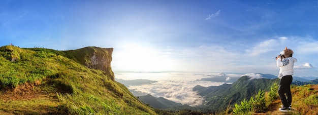 Panorama de la naturaleza del hermoso paisaje de la salida del sol en el pico de la montaña con el cielo brillante de la niebla de la nube del sol y el turista de la mujer están tomando fotos en invierno en el parque forestal de Phu Chi Fa, provincia de Chiang Rai, Tailandia