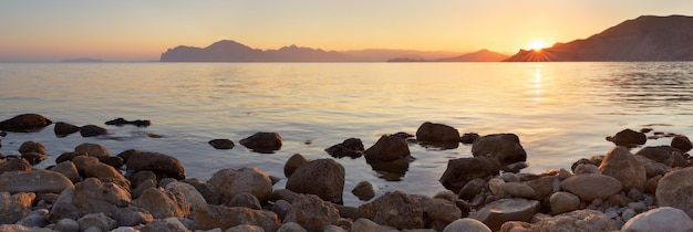 Panorama del paisaje al atardecer. Orilla del mar con piedras. Una cálida tarde de verano