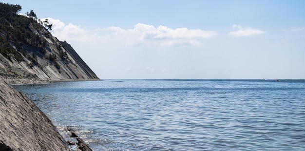 Foto panorama del paisaje del mar. una pintoresca playa salvaje de piedra al pie de los acantilados y un cielo azul brillante con nubes.