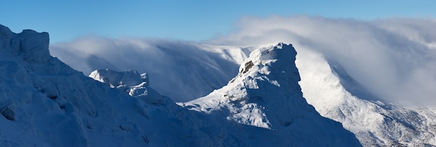 Panorama del paisaje de montañas de invierno con rocas en la nieve y las heladas. Cordillera en las nubes. Cárpatos ucranianos