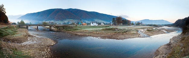 Panorama del pueblo de montaña de la mañana brumosa del otoño (Kolochava, Cárpatos, Ucrania). Imagen de puntada de tres disparos.