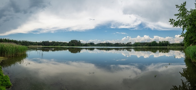 Panorama reflejado cielo azul con nubes blancas y bosque en la superficie de un lago