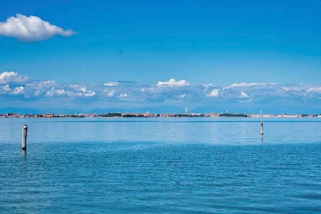 Panorama de la superficie del agua de mar con poste de madera junto con edificios de la ciudad en el fondo