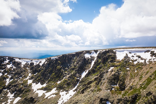 Panorama ultra amplio del horizonte. montañas cubiertas de nieve, claro con un verde bosque de coníferas contra el cielo azul.