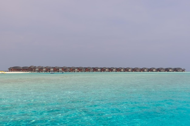 Panorama von Wasservillen (Bungalows) und Holzsteg am tropischen Strand auf den Malediven im Sommer