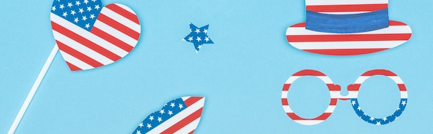 Panoramaaufnahme einer aus Papier geschnittenen dekorativen Brille, Hutlippen, Stern und Herz aus US-Flaggen auf Blau