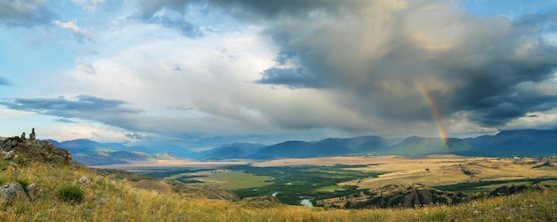 Panoramablick auf das Bergtal, Gewitterwolke mit Regenbogen